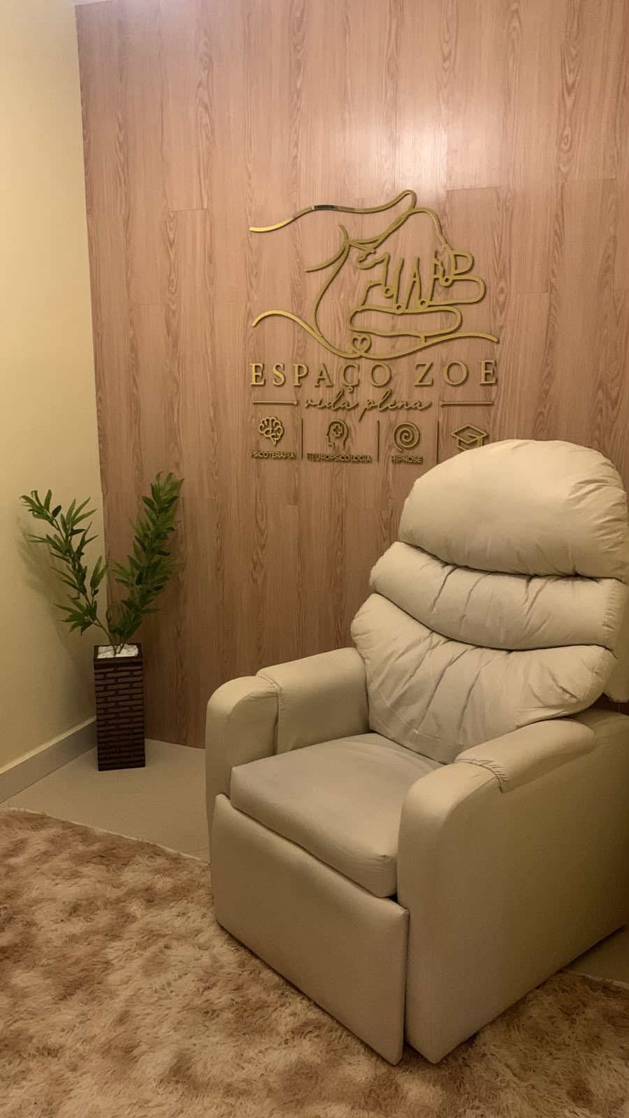 Sala de atendimento do Espaço Zoe, com poltrona clara e o logotipo dourado na parede